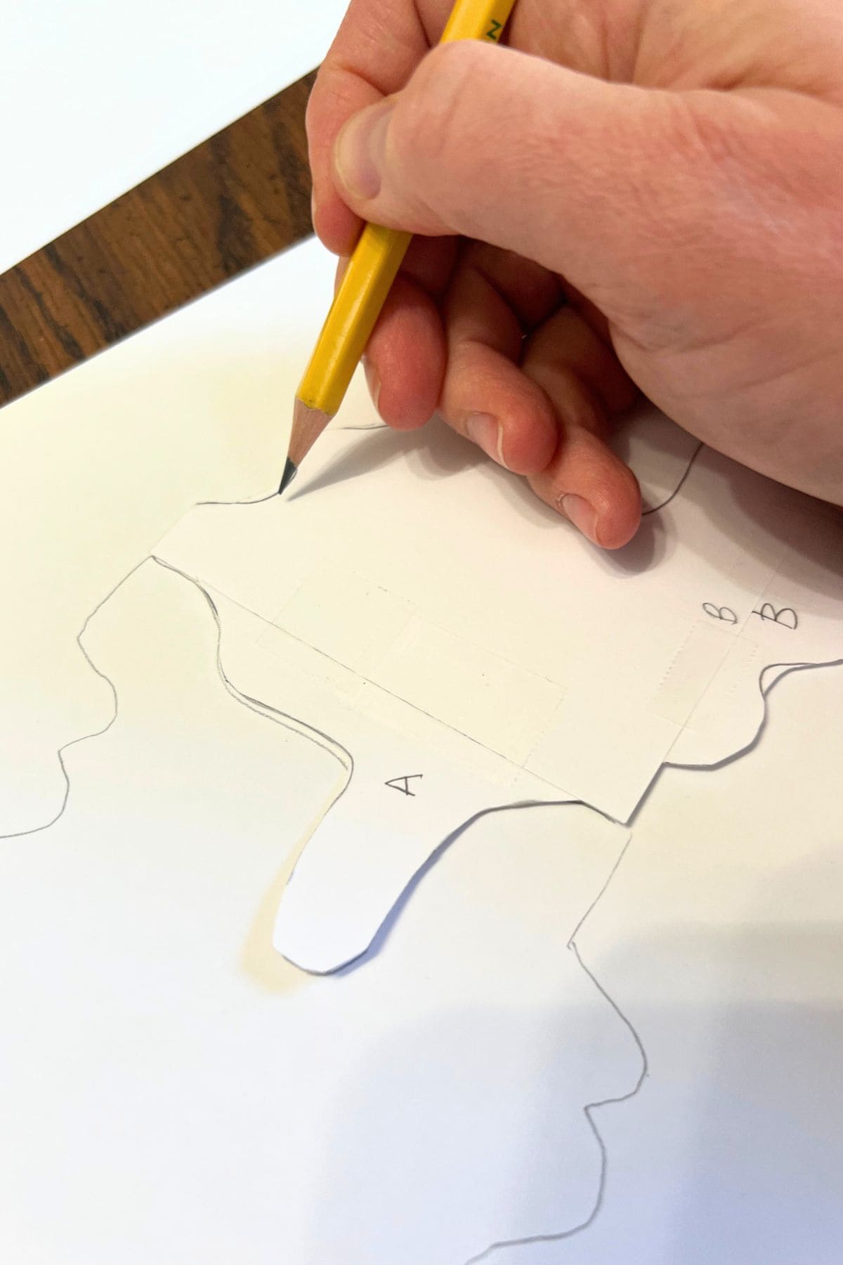 hand holding a pencil and drawing around more shapes on the paper.