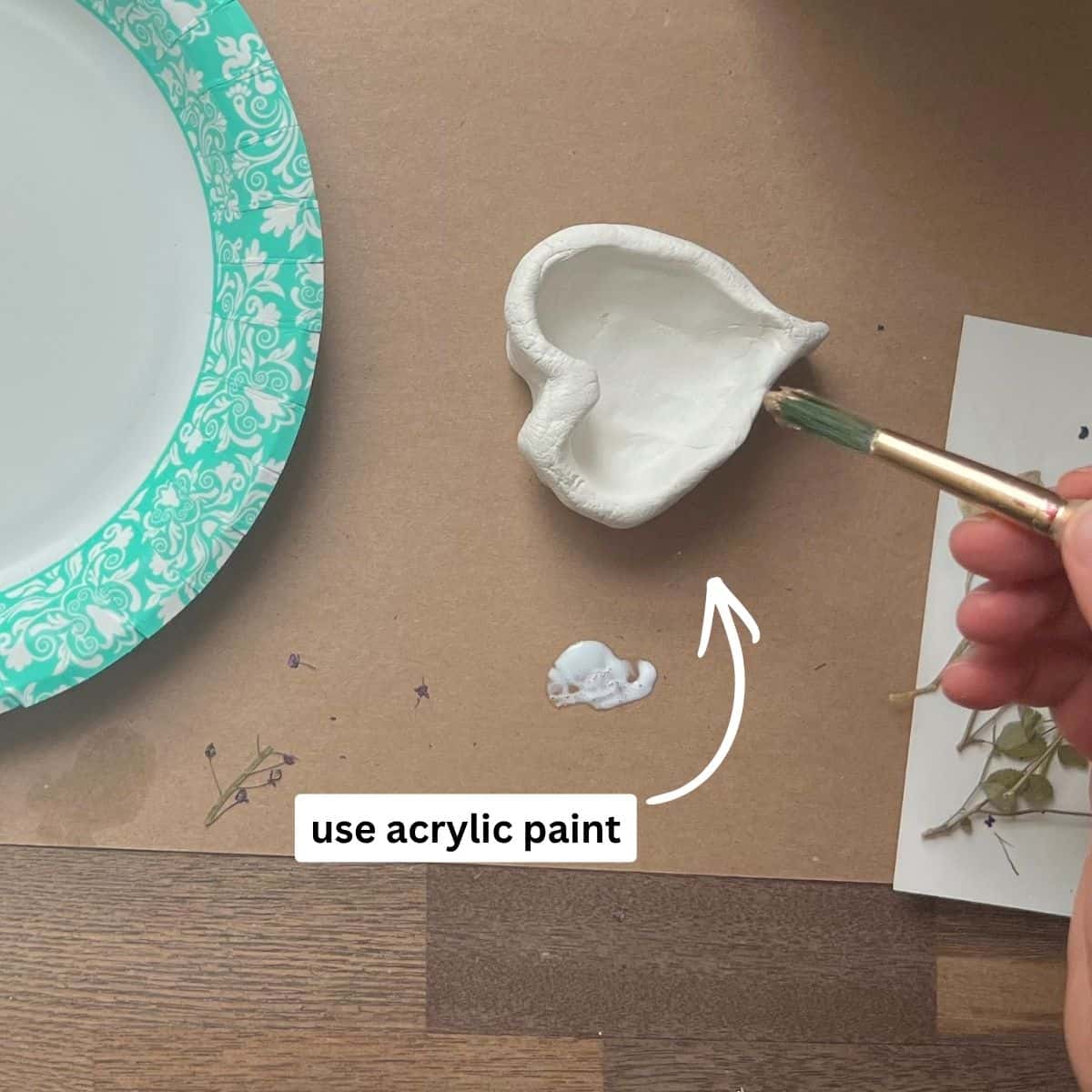 hand holding paint brush with gold paint on it being applied to clay dish.