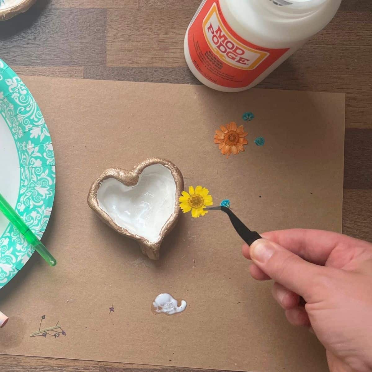 hand holding tweezers with dried yellow flower.
