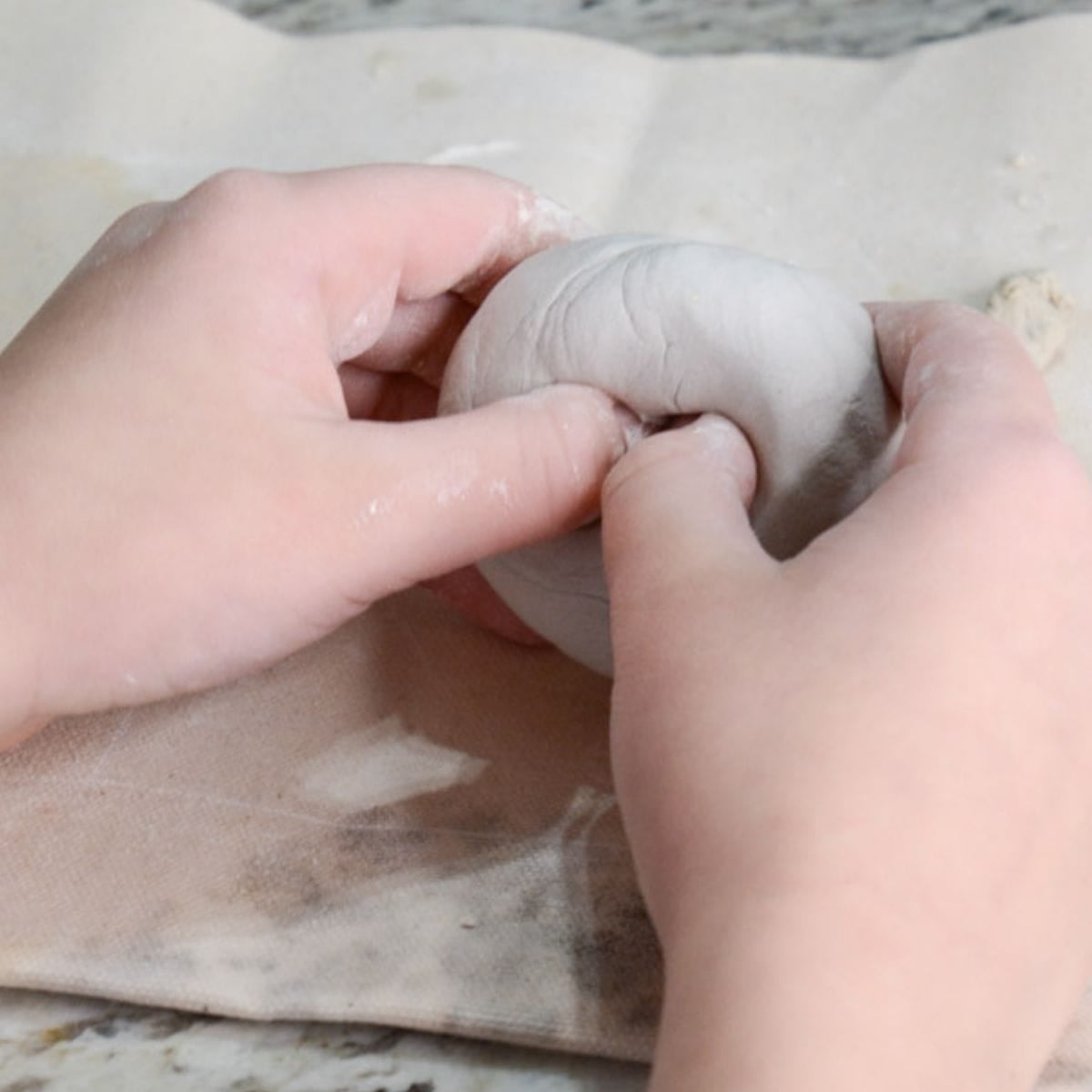 child's hand placing thumbs into clay.