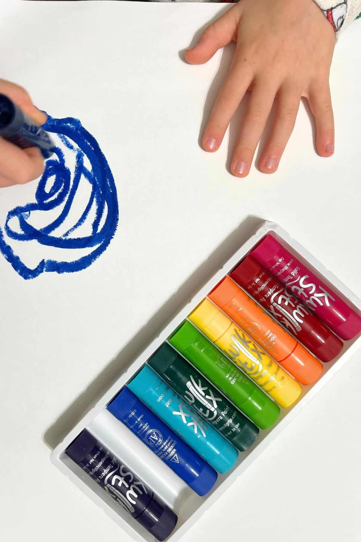 child's hands using paint sticks on a paper.