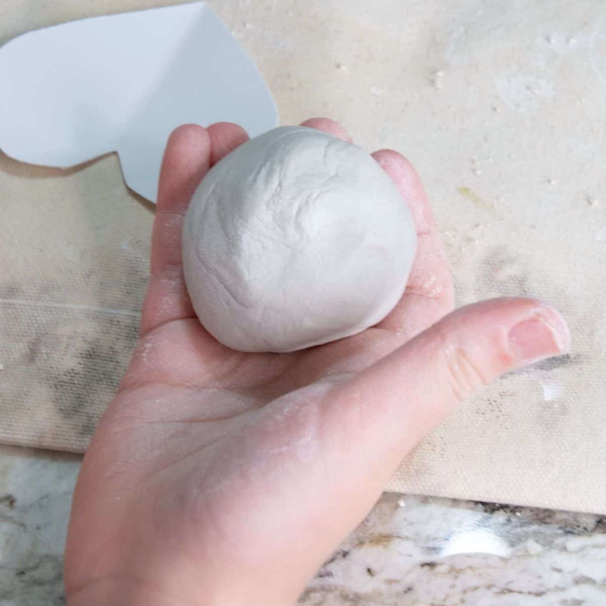 child's hand holding a ball of  air dry clay.