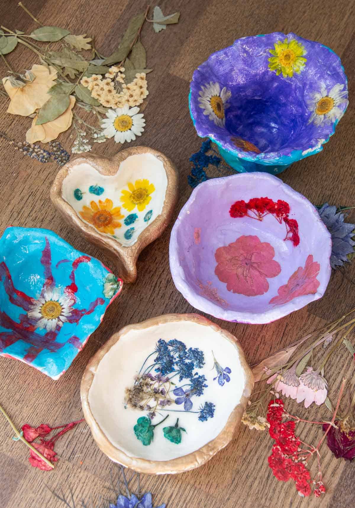 5 pressed flower clay dish art projects on a table.