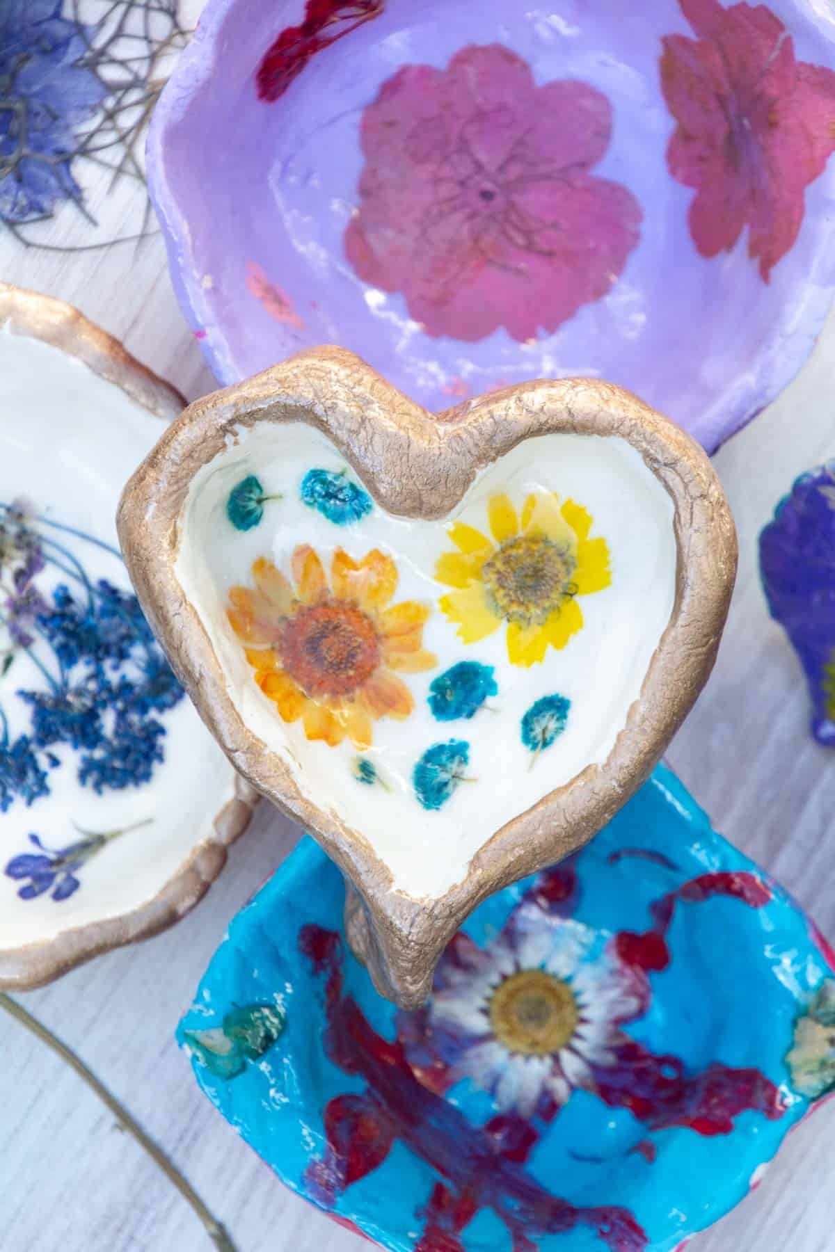 heart clay flower dish with yellow flower in the middle on top of other pressed flower clay dishes.
