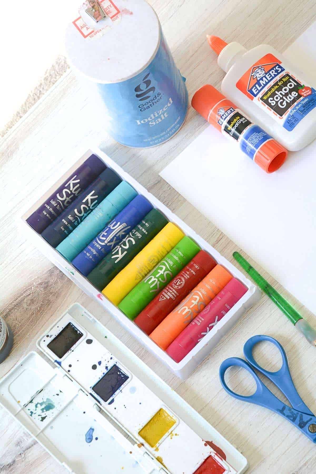 paint sticks, glue, salt, scissors, watercolor paint and paper on a table.